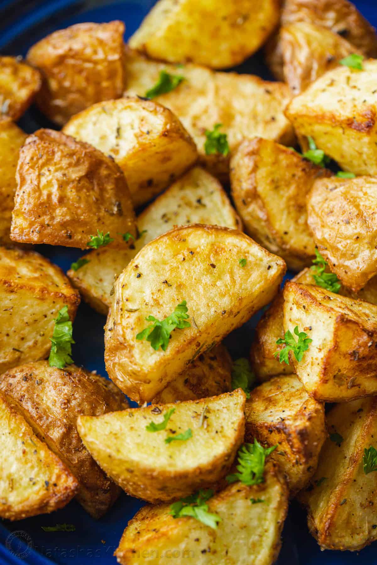 These easy, 20-minute air fryer roasted potatoes are ready in half the time as oven-roasted potatoes and they turn out just as crispy! Close up of air fryer roasted potatoes garnished with parsley.