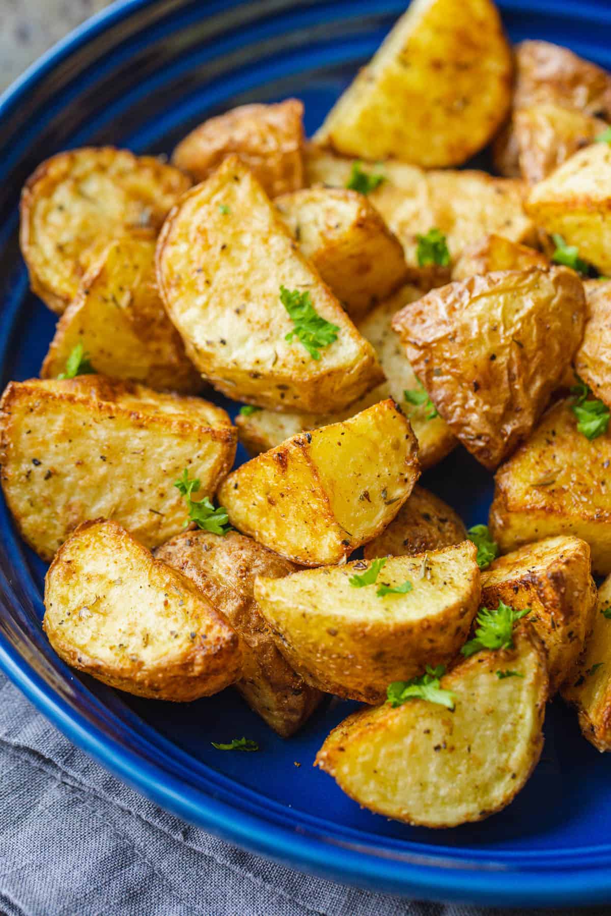 These easy, 20-minute air fryer roasted potatoes are ready in half the time as oven-roasted potatoes and they turn out just as crispy! Close up of air fryer roasted potatoes on a blue platter, garnished with parsley.