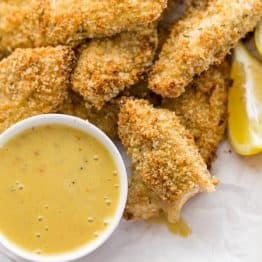 A plate of baked breaded chicken strips with a honey mustard dip beside them