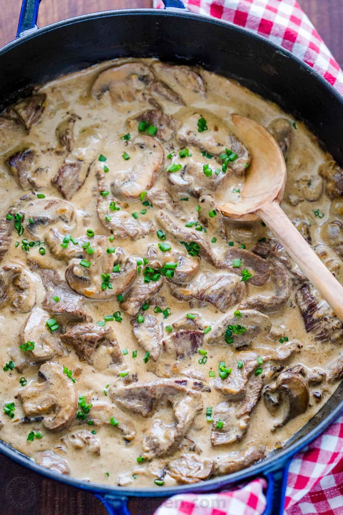 Classic Beef Stroganoff with tender strips of beef and mushrooms in an creamy Stroganoff sauce, served over noodles. An easy, one-pan, 30-minute recipe! #beefstroganoff #beefstroganoffrecipe #stroganoff #beef #beefrecipes #dinner #onepandinner #natashaskitchen Beef Stroganoff in a pan garnished with chives
