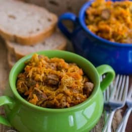 A green and blue bowl with braised cabbage with beef and bread in the background