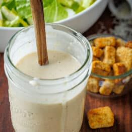 Homemade Caesar salad dressing in a jar with croutons and romaine lettuce