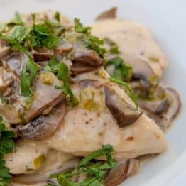 A white plate with chicken with mushroom white wine cream sauce