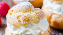 Cream puffs served dusted with powdered sugar surrounded by raspberries