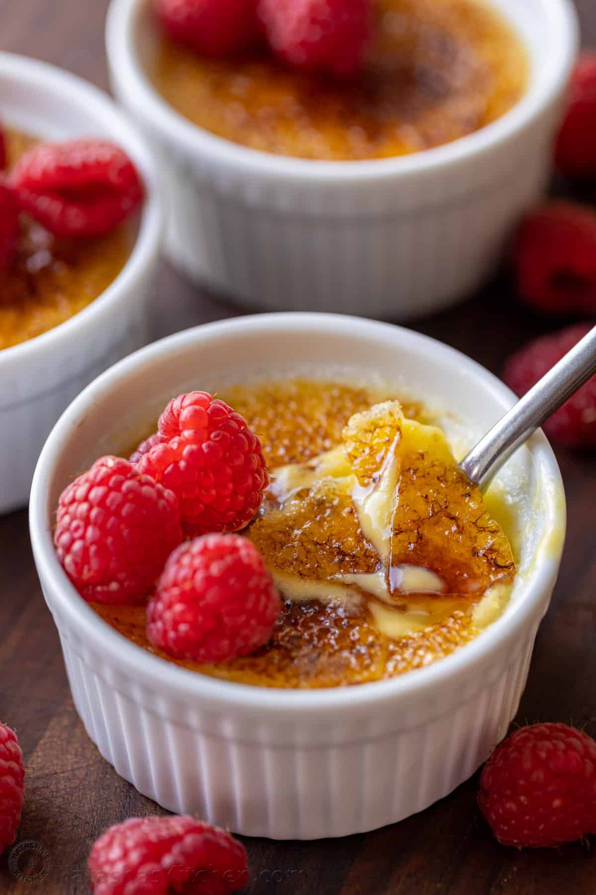 Creme Brulee is a creamy, indulgent dessert made with only 5 ingredients! Here's how to make a restaurant-quality vanilla creme brulee. Creme brulee topped with raspberries, with the caramelized sugar topping cracked with a spoon.