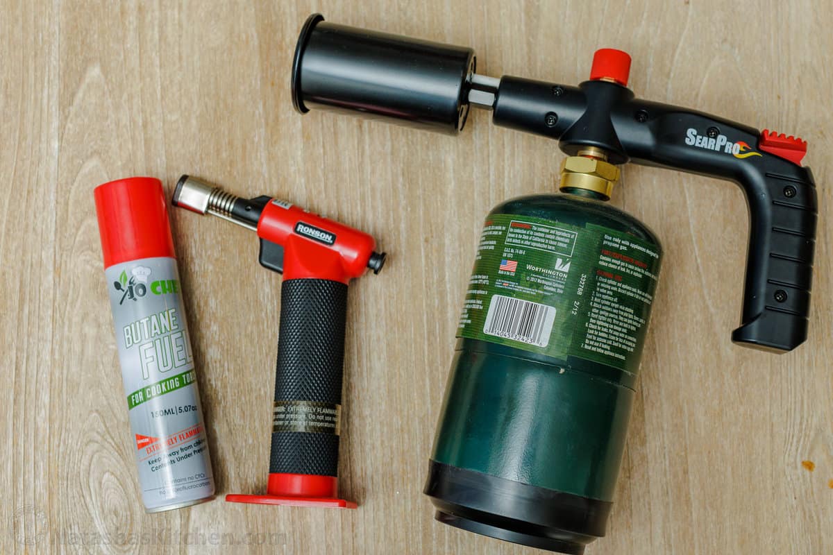 Creme Brulee is an easy dessert recipe made with just 4 ingredients! Learn how to make homemade creme brulee that tastes restaurant-quality. Overhead view of large and small kitchen torches on a countertop next to a can of butane.