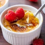 Creme brulee topped with raspberries, with the caramelized sugar topping cracked with a spoon.