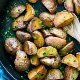 A skillet with crisp sautéed red potatoes and a wooden spoon