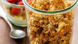 healthy Homemade granola in a glass jar near a yogurt parfait with raspberries and a spoon