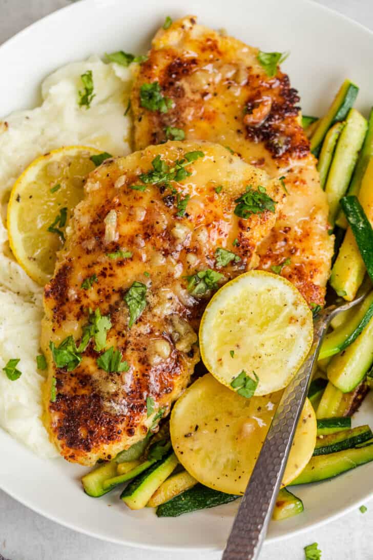 Parmesan crusted chicken breast on a bed of mashed potatoes and zucchini in a lemon butter sauce topped with greens.
