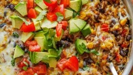 Mexican Ground Beef and Rice Skillet garnished with fresh diced tomatoes, avocado, and cilantro. Ready to serve with a spoon.