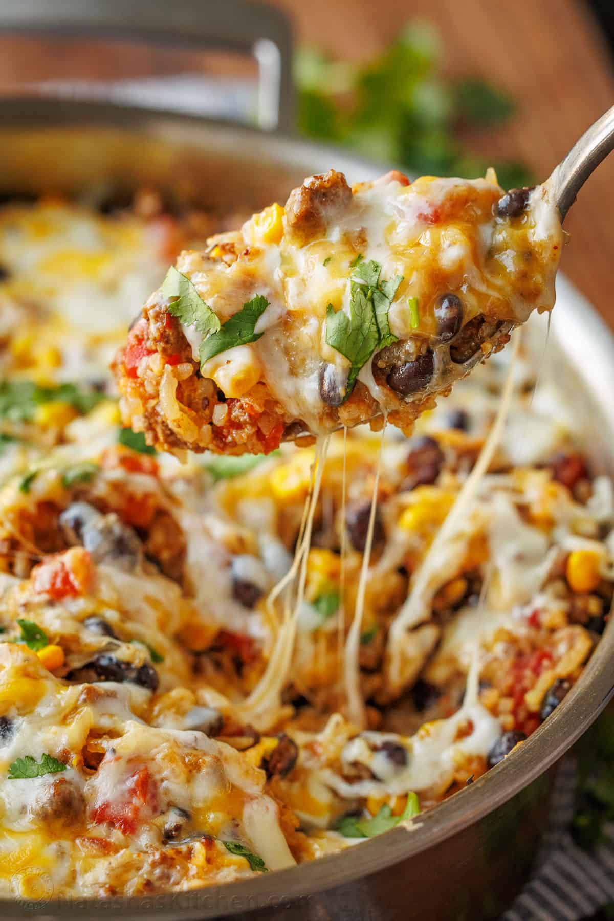 Mexican Beef and Rice Skillet is a quick, 30-minute meal—seasoned beef, loaded rice, and gooey melted cheese. The perfect one-pan wonder! A serving spoon loaded with Mexican Ground Beef and Rice Skillet, showcasing the Mexican cheese pulls.