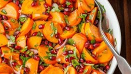 Persimmon pomegranate salad in a white bowl with serving spoon.