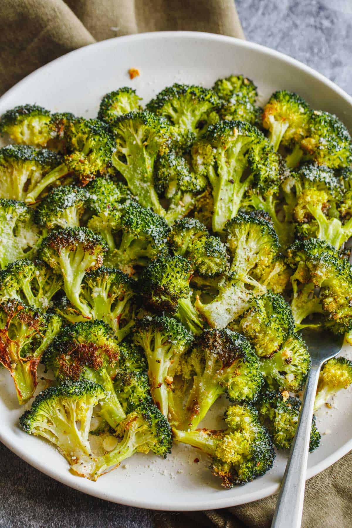 The Best Roasted Broccoli Recipe with crisp golden edges. Tossed with olive oil and perfectly seasoned for an easy, excellent broccoli side. Oven roasted broccoli florets on a plate with serving fork