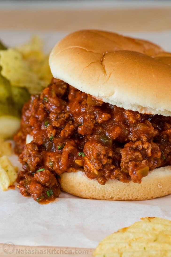 The BEST homemade sloppy joes recipe that is easy to make and loaded with flavors from the rich and flavorful tomato sauce. Sloppy joe sandwich on a plate with chips and pickles.