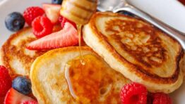 Sourdough discard pancakes stacked on a plate with fresh berries and drizzled honey