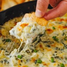 Cheesy spinach and artichoke dip scooped onto a chip with cheese pulls