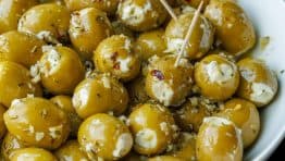 Stuffed green olives with white Boursin cheese, in a white bowl. Some olives have toothpicks for serving.